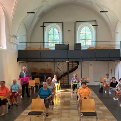 Bild vergrößern: Mehrere Senioren auf Sthlen in einer ehemaligen Kirche, im Hintergrund die Empore.