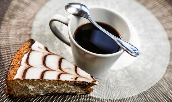 Bild vergrößern: Ein Stck Kuchen und eine Tasse Kaffee mit Kaffeelffel.