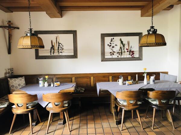 Bild vergrößern: Zwei Bilder im Hintergrund an der Wand, davor stehen zwei Tische mit Sthlen aus Holz. Die Tische sind mit einer Decke und Vasen gedeckt.