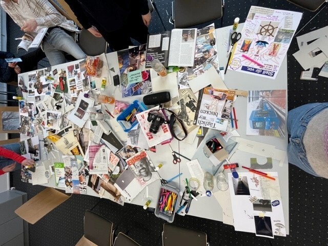 Bild vergrößern: Ein Tisch auf dem Viele verschiedene Zeitschriften, Programmhefte, Fotos und allerlei buntes Papier liegen.