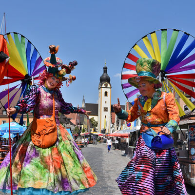 Bild vergrößern: Zwei als bunte Gaukler verkleidete Stelzenknstler auf dem Schwandorfer Marktplatz.
