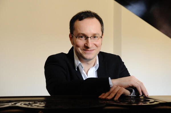 Bild vergrößern: Portrtaufnahme des Pianisten Christian Seibert. Er sitzt an einem Klavier und lchelt in die Kamera.