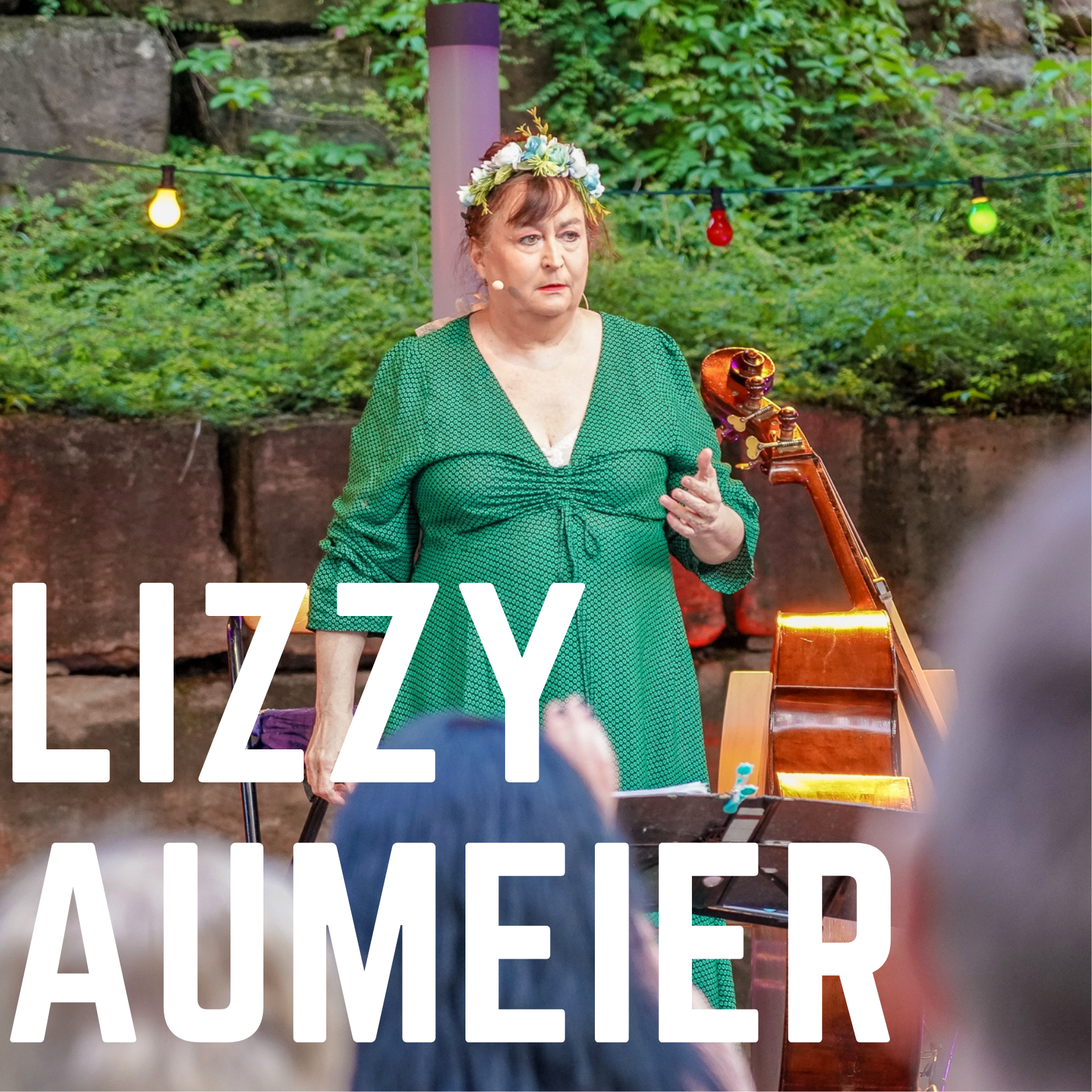 Bild vergrößern: Der Name der Knstlerin "Lizzy Auermeier" ist in weien Blockbuchstaben auf dem Foto zu sehen. Im Hintergrund ist die Kabarettistin Lizyy Aumeier auf der Open-Air Bhne des Kultursommer 2021 zu sehen.