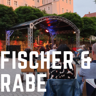 Bild vergrößern: Die Aufschrift "Fischer & Rabe" in weien Druckbuchstaben ist auf dem Foto abgebildet. Im Hintergrund ist die Musikgruppe Fischer und Rabe auf der Open-Air Bhne des Kultursommer 2021 zu sehen.