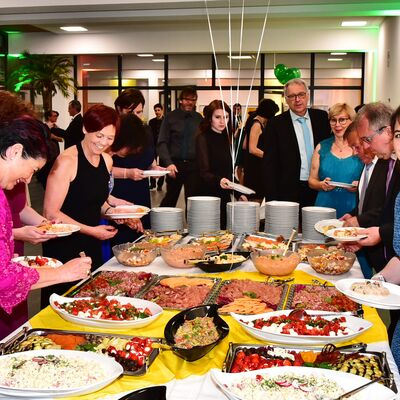 Foto des vielfltigen Buffets und lchelnden Menschen, die sich etwas zu essen nehmen.