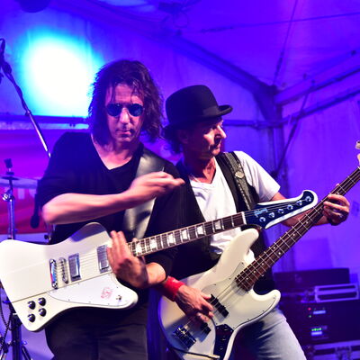 Bild vergrößern: Foto zweier Gitarristen, die auf einer Bhne performen. Die Hintergrundbeleuchtung ist blau.
